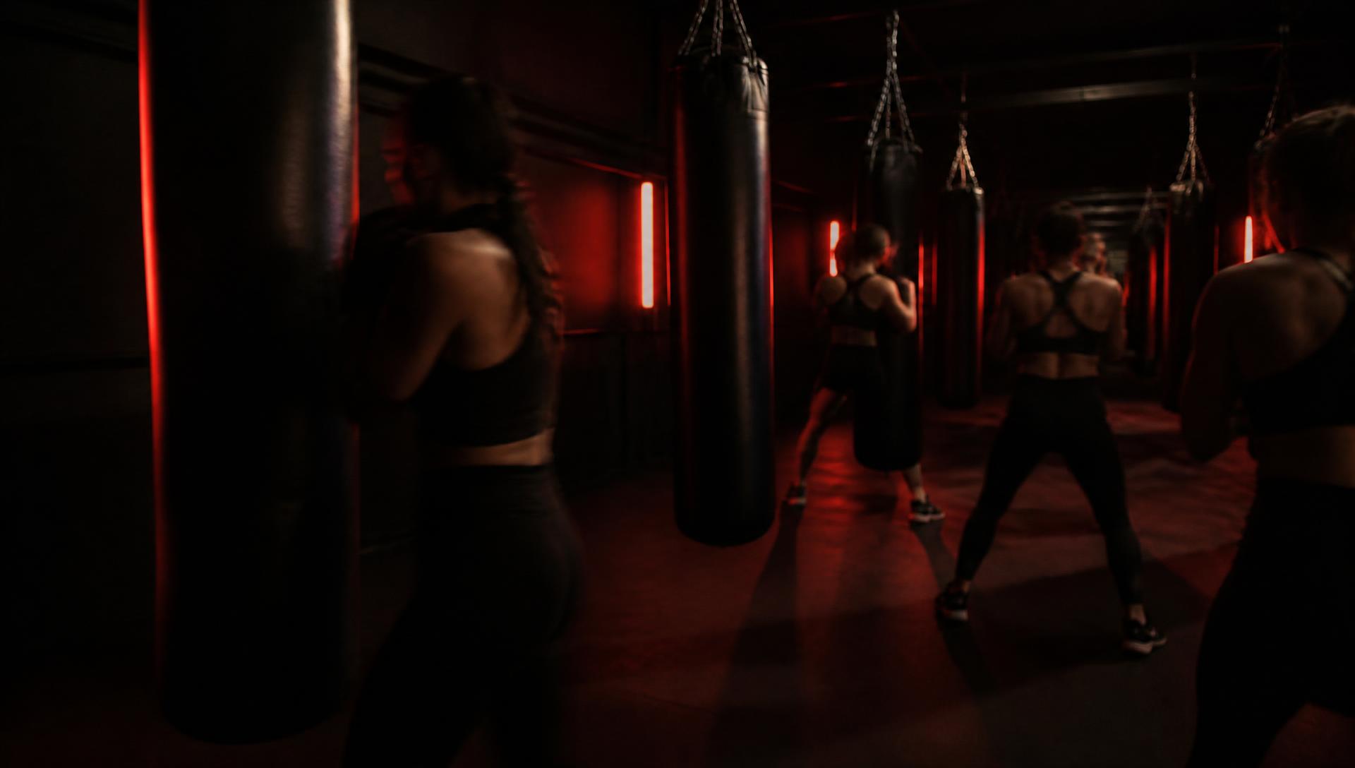A dark studio full of people training together on heavy bags under red light