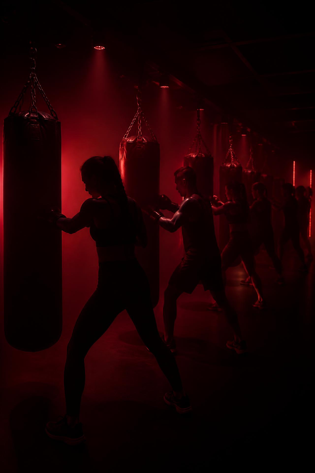 Dark studio with hanging heavy bags lit in deep red while a group trains